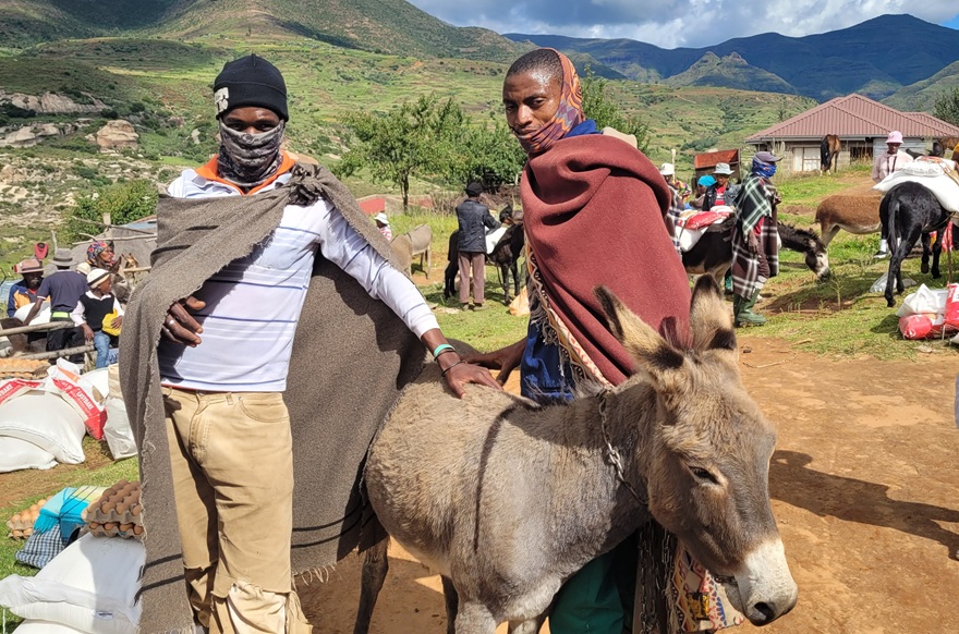 Two local villagers wearing blankets post in front of a donkey as they prepare to assist in transporting food rations.