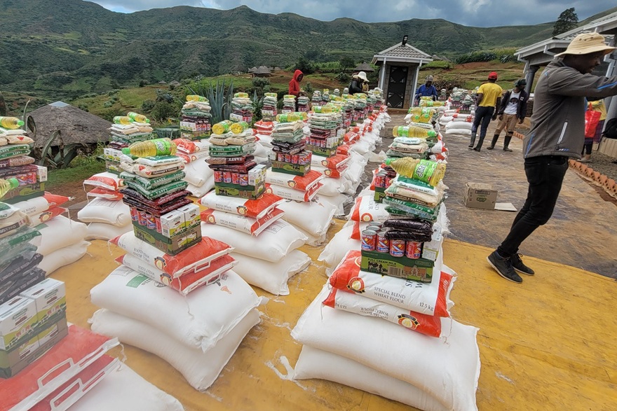 Neat stacks of monthly rations sitting outside with green mountains in the background.