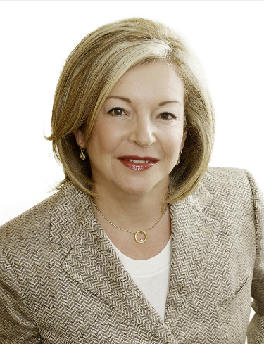 Margaret O'Sullivan, a white woman with blonde hair smiles while wearing a white shirt and a beige suit jacket