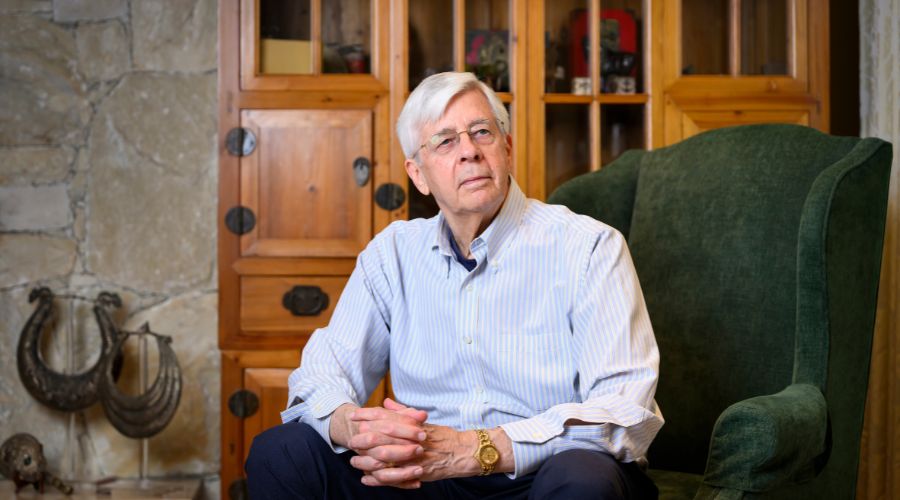 David Nesbitt sits on a green chair, appearing contemplative, surrounded by light wood furniture.