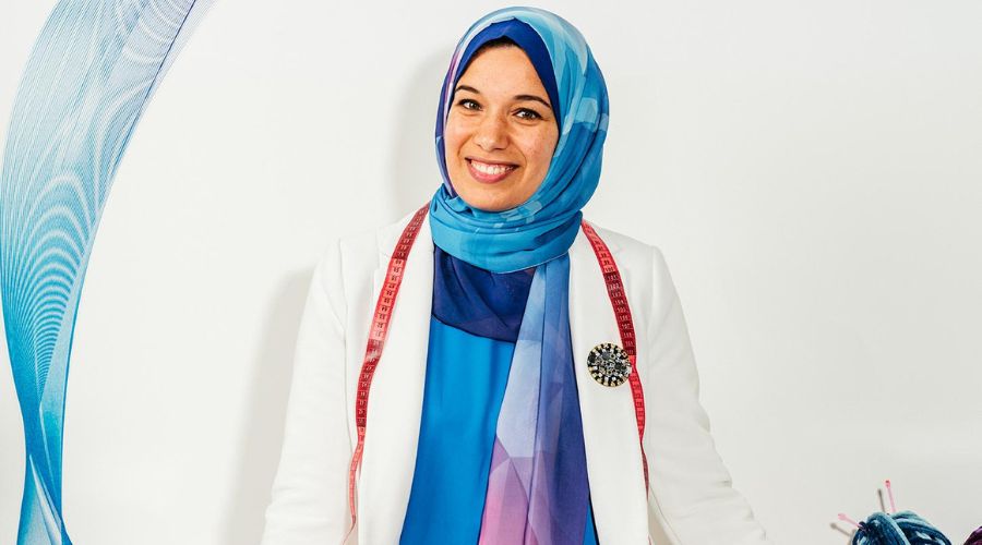 Sara Nabil stands confidently with a warm expression and a measuring tape on her shoulders. 