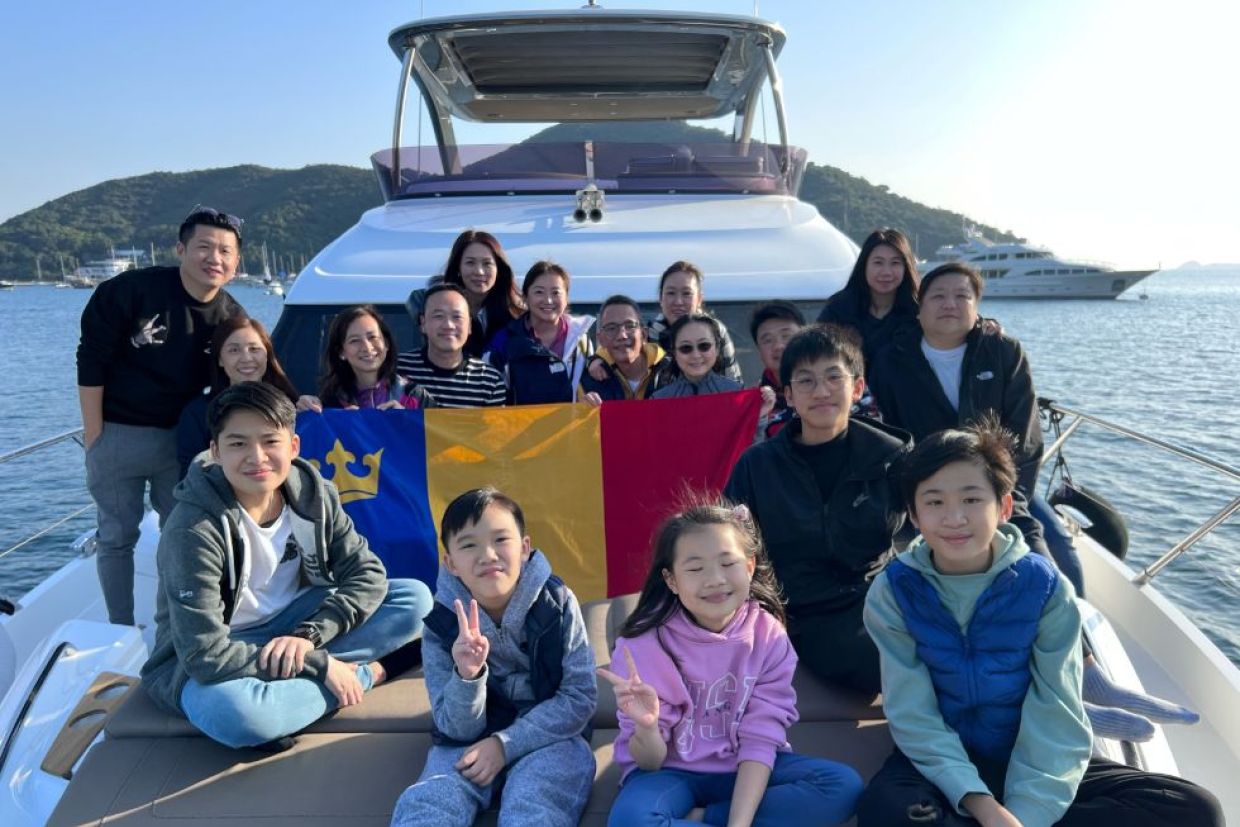Alumni and their families holding the Queen's tricolour flag on a boat.