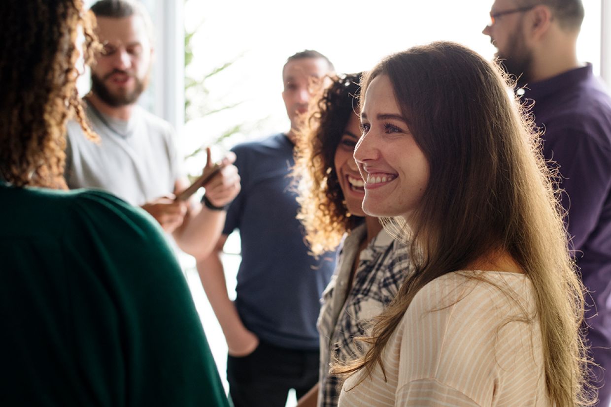 A person in conversation smiles. Others mingle in the background casually.