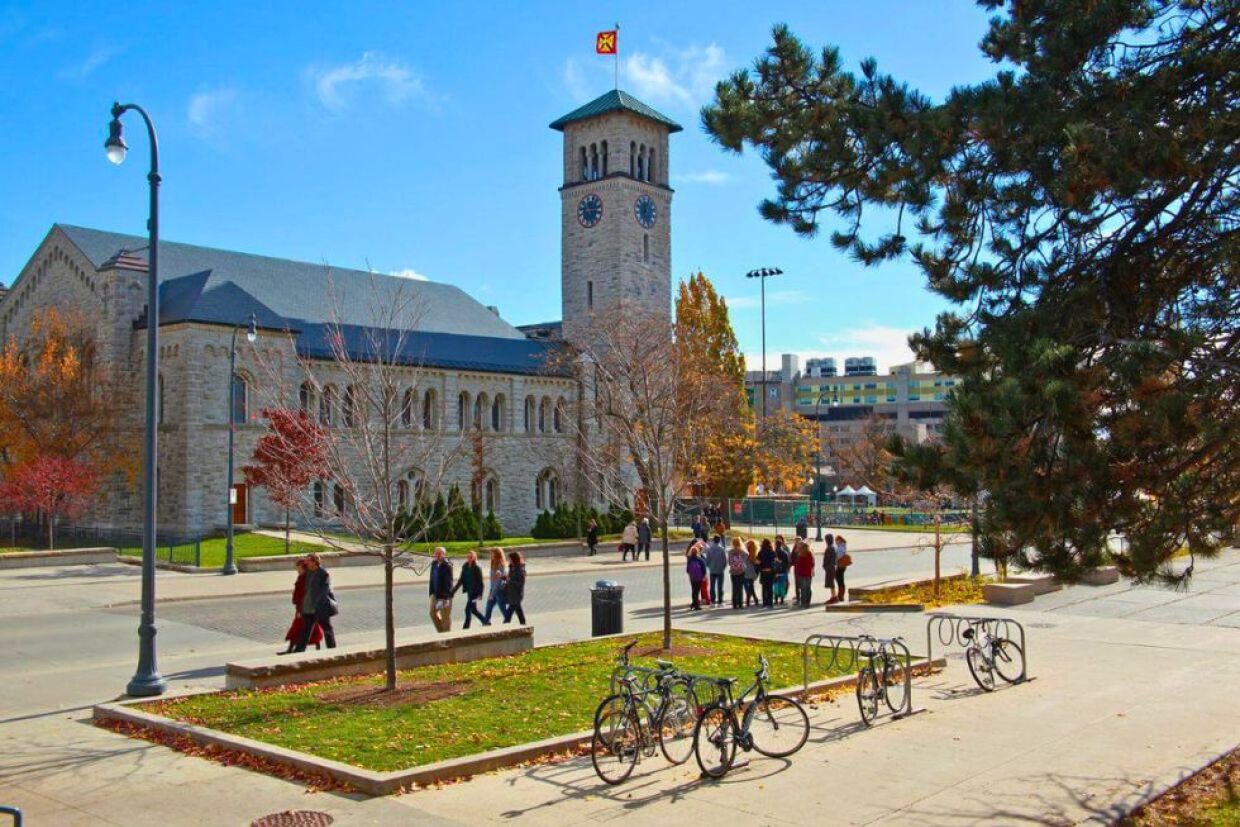 A view of Grant Hall Tower at Queen's University, featuring a tall limestone clock tower amidst fall preparations for Homecoming.