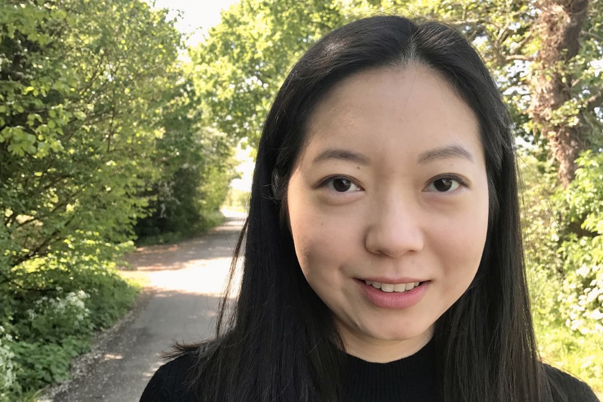 Margaret Zou, Artsci’13, stands with long black hair in front of a road, looking towards the distance.