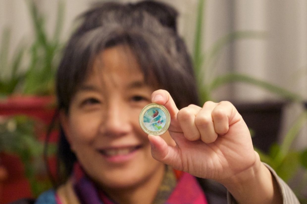 Emily Chen, BFA’98, holds the 50-cent holiday coin she illustrated for the Royal Canadian Mint. It showcases a Christmas scene. 