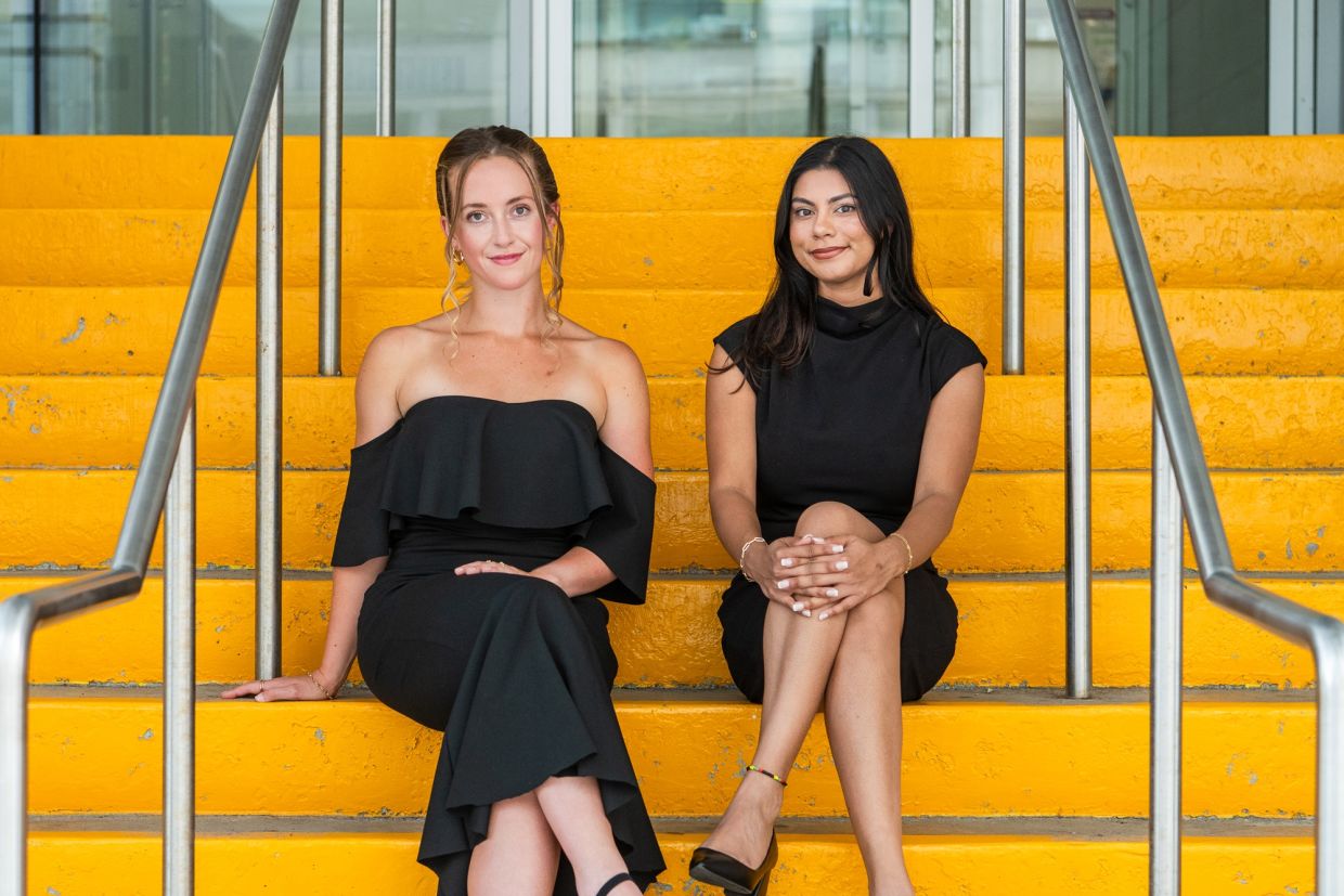 Hailey Rodgers and Meera Mahadeo sitting on yellow stairs. 