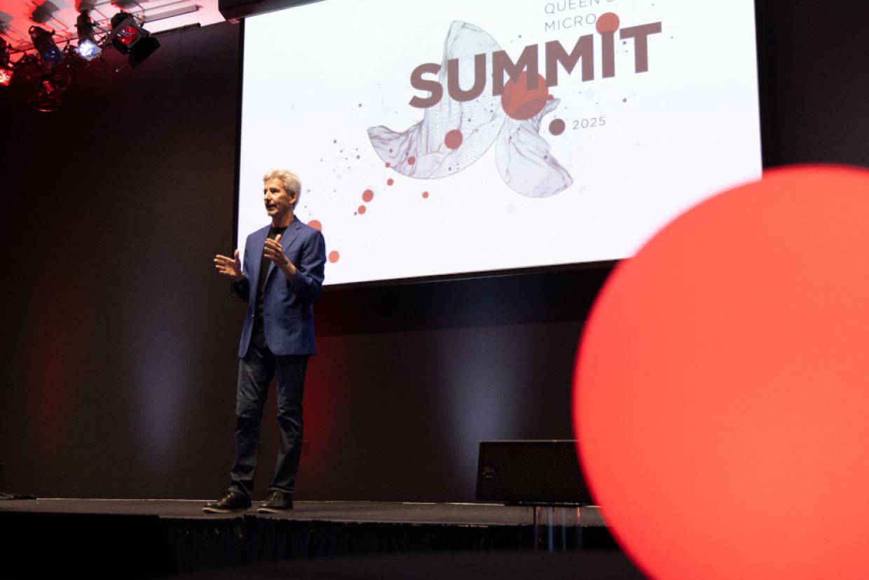 Queen's researcher stands on stage to present at Queen's micro summit.