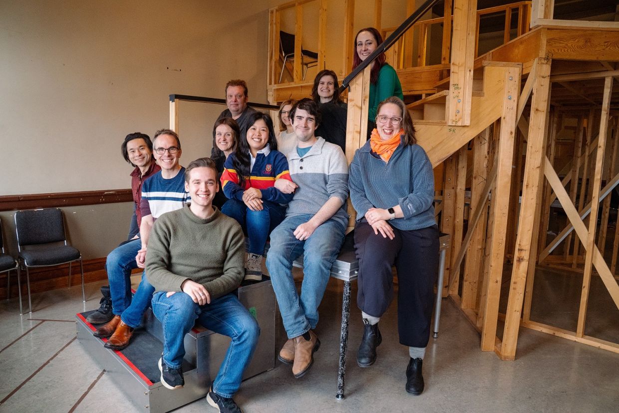 Eleven smiling alumni pose on the staircase of a set at Stratford Festival.
