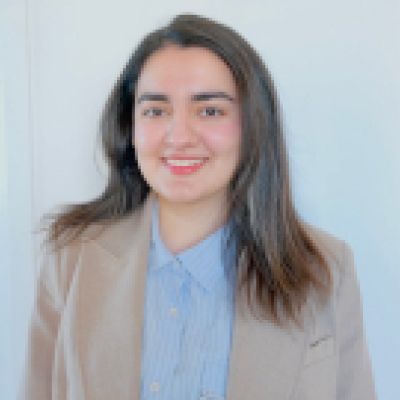 Ghazal smiling. She is wearing a blue shirt and tan jacket 