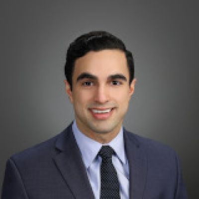 Kahir smiling. He is wearing a blue shirt, jacket and tie 