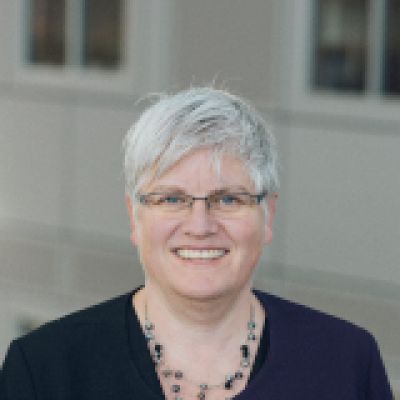 Cheryl Carver smiling wearing glasses, a blue shirt and jacket