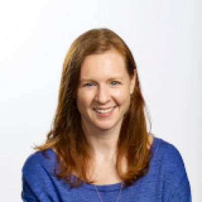 Julie smiling. She is wearing a blue shirt and gold necklace 