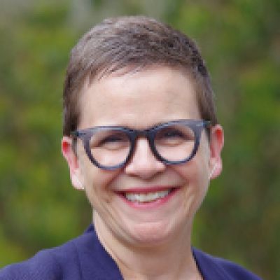 Kelly smiling. She is wearing glasses a white shirt and purple jacket 