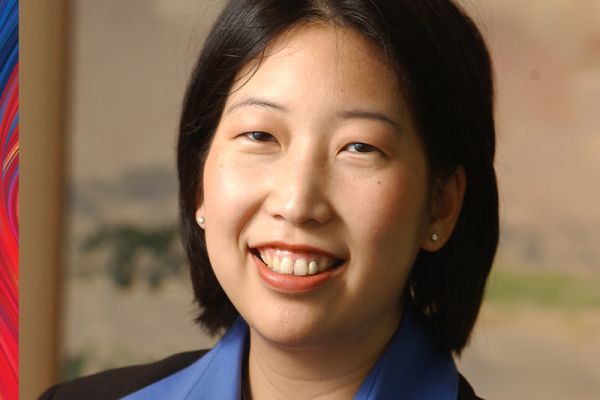 Elaine Wu smiling wearing a blue collared shirt, black jacket, with shoulder length black hair
