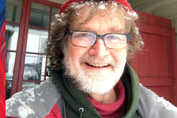 David Field smiling wearing a red and grey coat, red hat and glasses