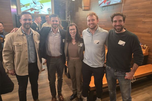 Group of people smiling to the camera and wearing business casual outfits with a restaurant on the background.