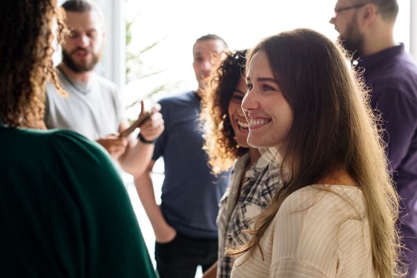 A person in conversation smiles. Others mingle in the background casually.