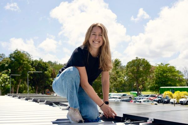 Meghan Wood, Com’18, smiles while kneeling on a rooftop showcasing an all-in-one solar battery pod.