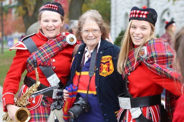 Dr. Pamela Frid posing at Homecoming between two members of Queen's Bands. 