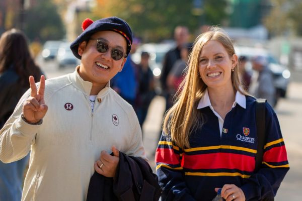 Two Queen's students smiling and posing together for a photo on a bustling street.