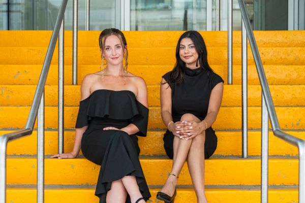 Hailey Rodgers and Meera Mahadeo sitting on yellow stairs. 