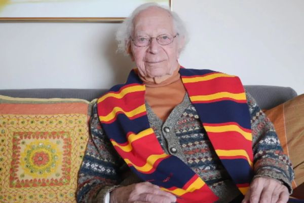 John Meisel sitting on a couch with a tricolour scarf around his neck.
