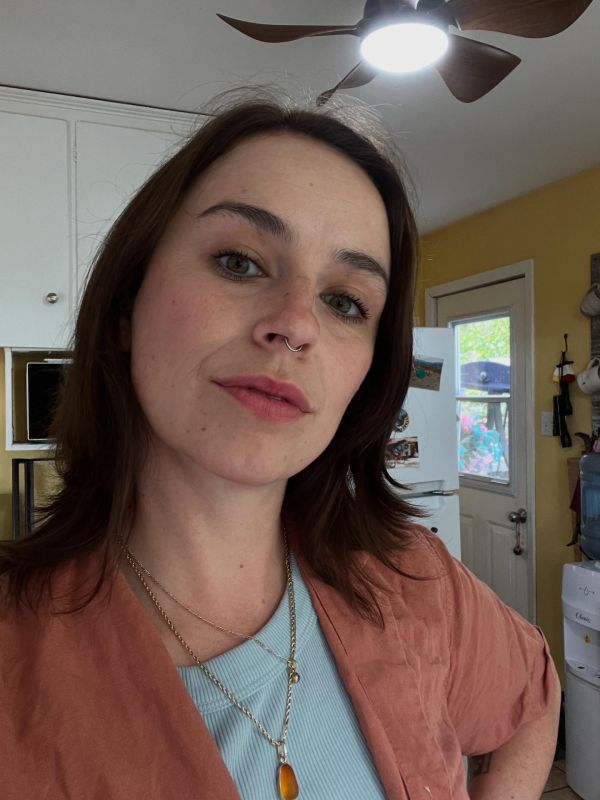 young woman with brown hair, wearing a coral shirt 