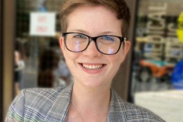 Devon Harvey smiles at the camera wearing a light grey plaid suit and black rimmed glasses.