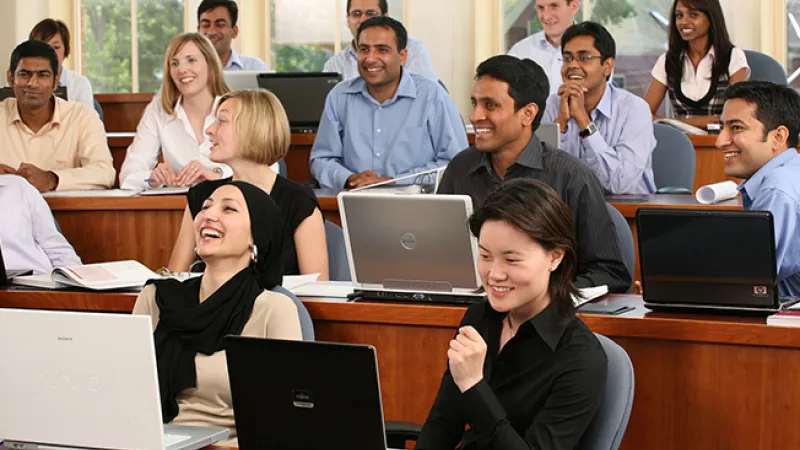 Photo of a group of students seated in a classroom with laptops and notebooks, listening during a lecture.