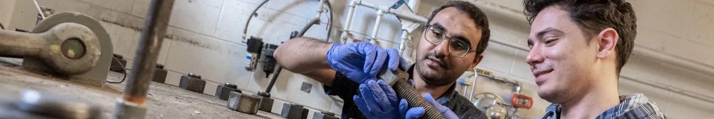 Two students operating a mechanical device in a laboratory setting.