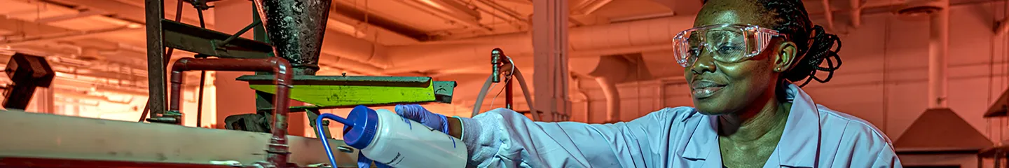 Student wearing a lab coat, exploring and testing liquid in a machine in an industrial setting.