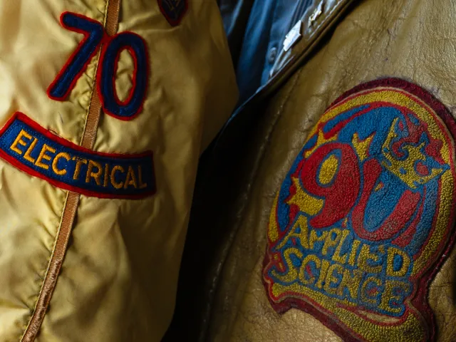 Close-up of vintage jackets displaying embroidered 70th Electrical and Applied Science patches, highlighting engineering tradition and alumni pride.